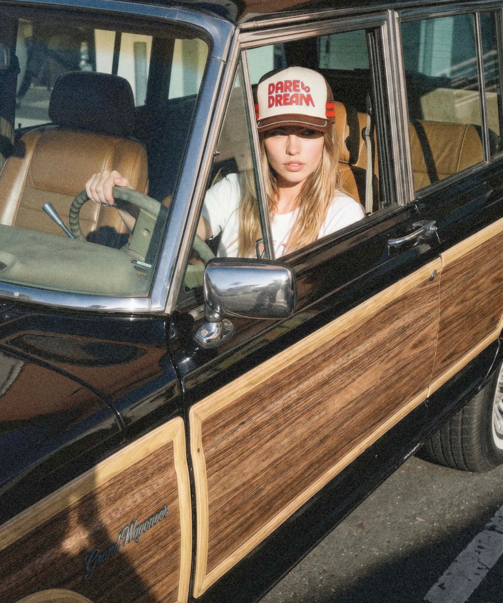 Dare to Dream brown vintage trucker hat worn by woman sitting in classic car, lifestyle shot