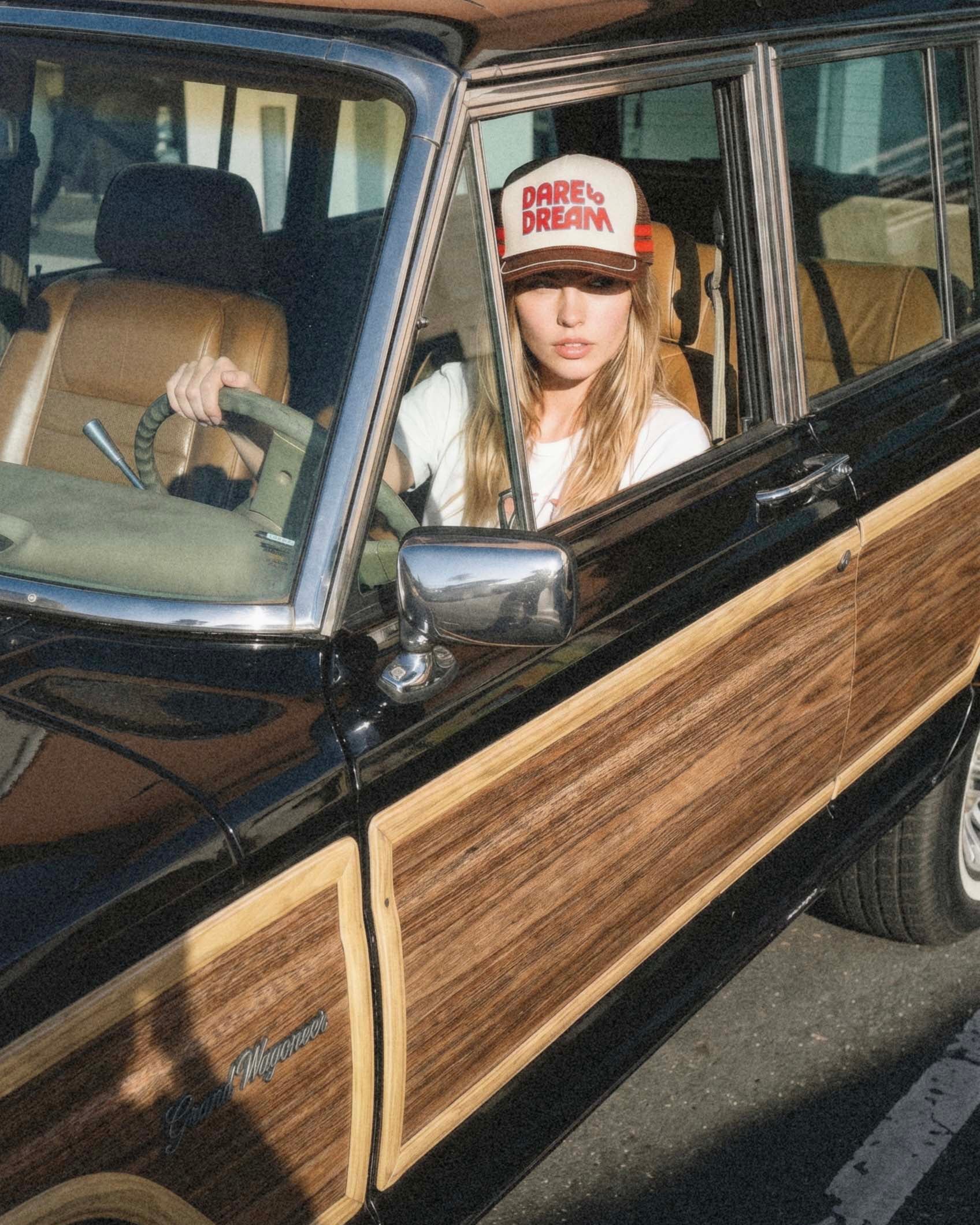 Dare to Dream brown vintage trucker hat worn by woman sitting in classic car, lifestyle shot