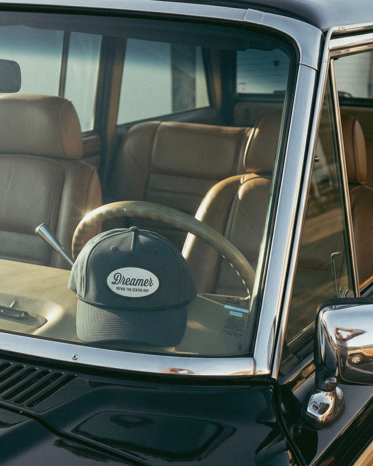 Dreamer Refuse the Status Quo navy trucker hat resting on vintage car dashboard, lifestyle product shot