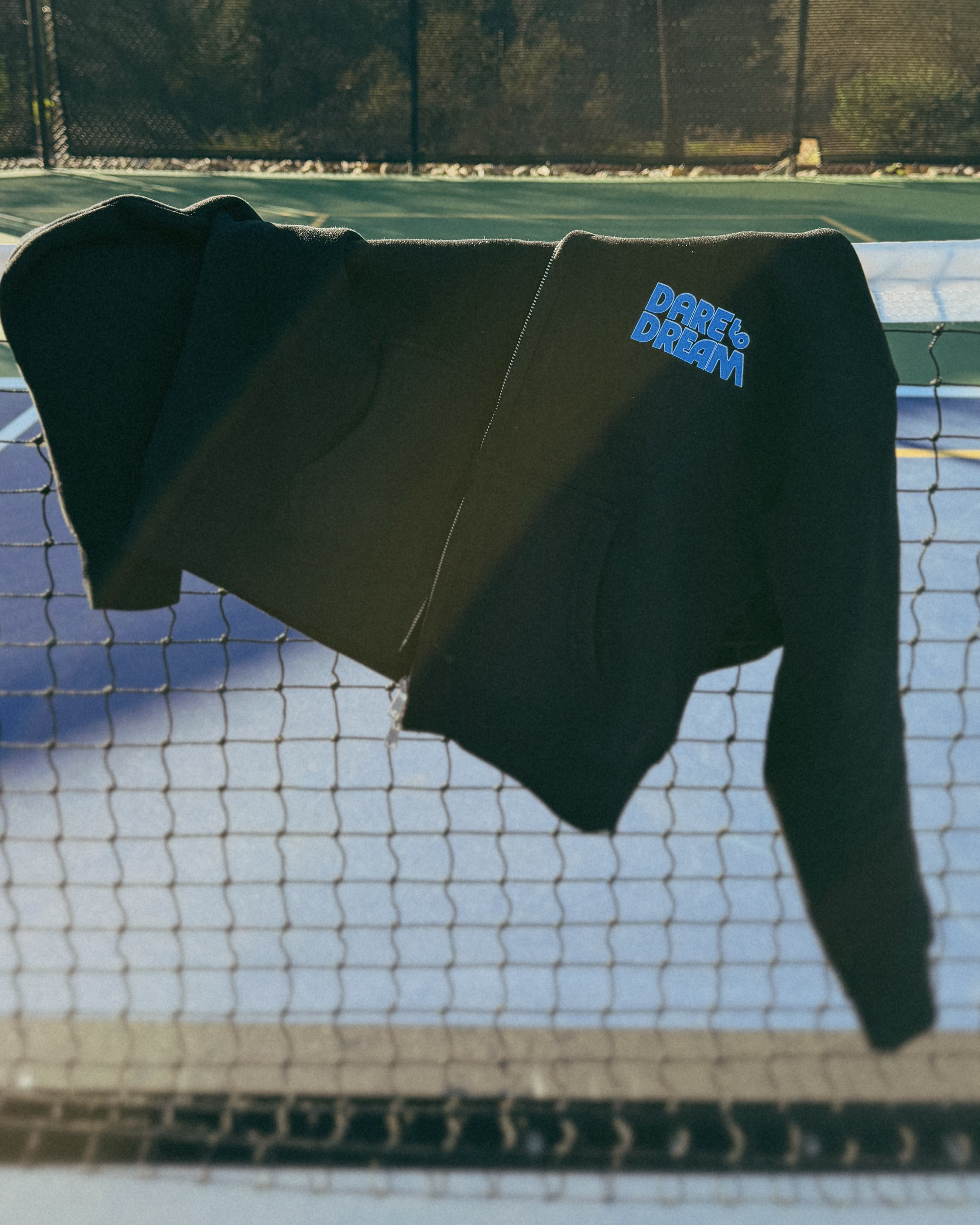 Black hoodie with 'dare to dream' text on a tennis court