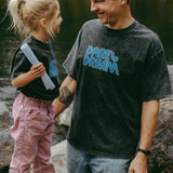 Man and child standing by a body of water, both wearing black t-shirts with 'Dare to Dream' text.