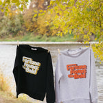 Two sweatshirts with text "fortune favors the bold" hanging on a clothesline by a body of water with autumn foliage.