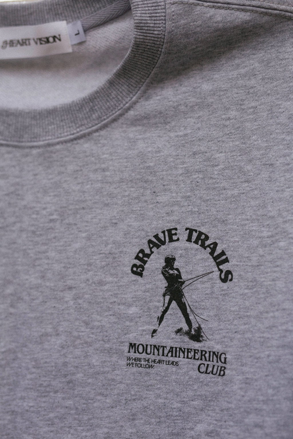 Gray sweatshirt with 'Brave Trails Mountaineering Club' logo on a close-up view
