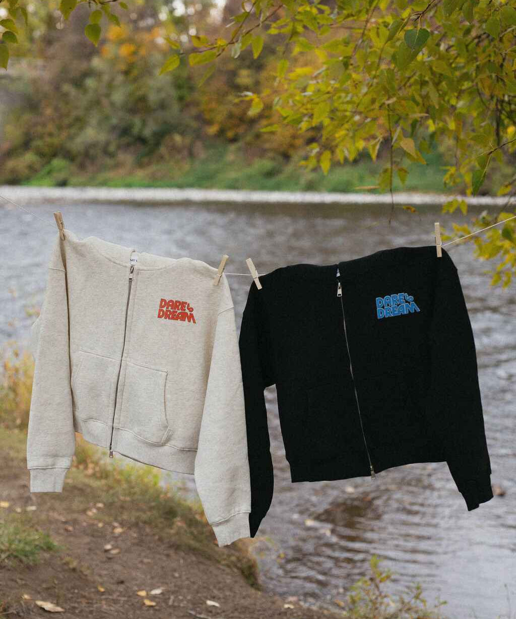 Two hoodies, one beige and one black, hanging on a clothesline with a natural background.