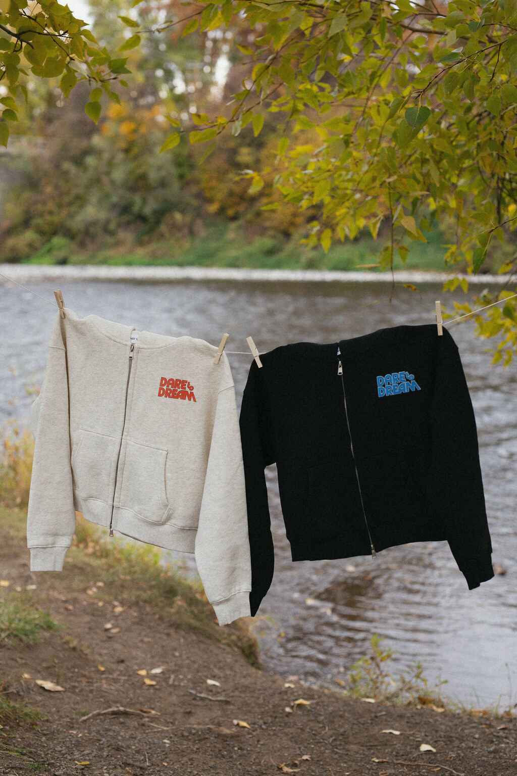 Two hoodies, one beige and one black, hanging on a clothesline with a natural background.