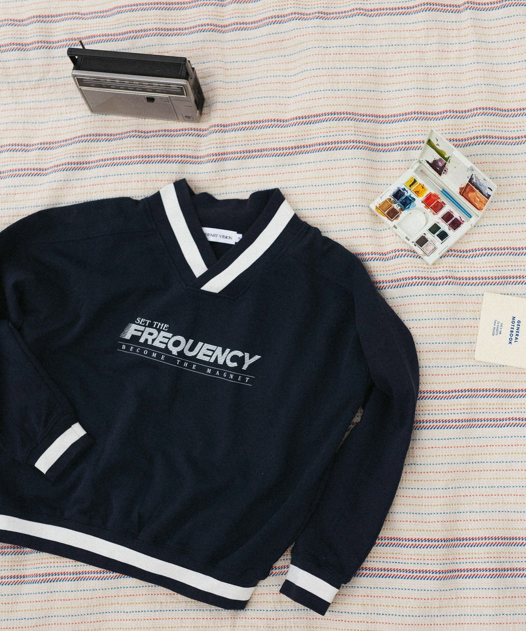 front of navy sweater with white text that says "set the frequency become the magnet" on a striped blanket background