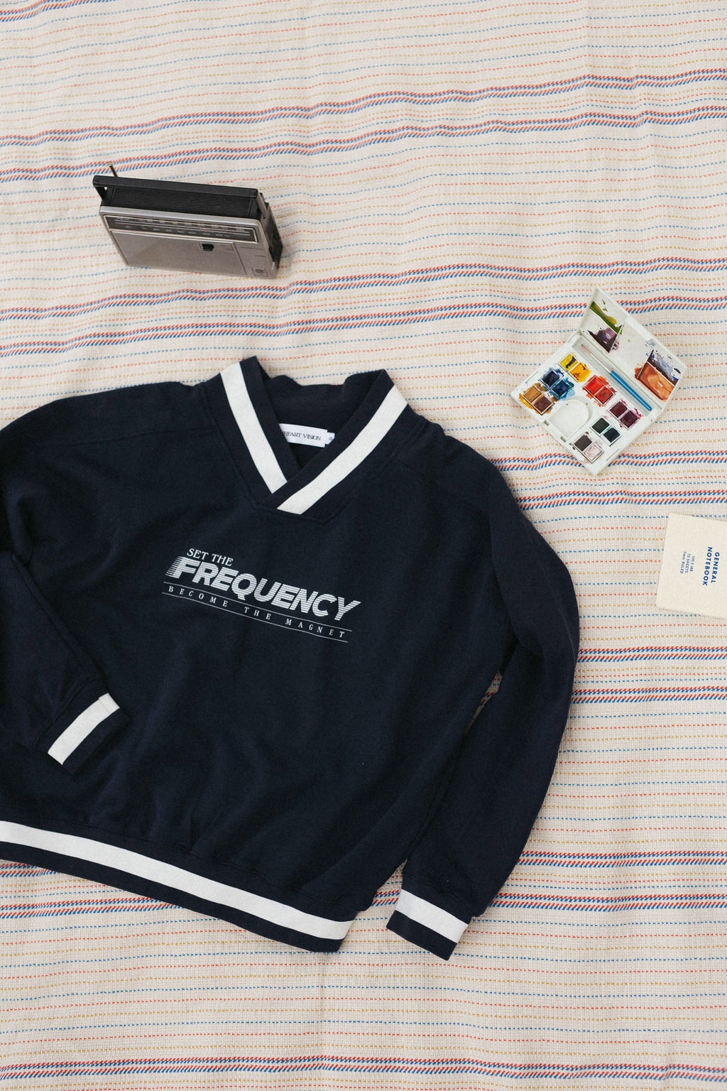 front of navy sweater with white text that says "set the frequency become the magnet" on a striped blanket background