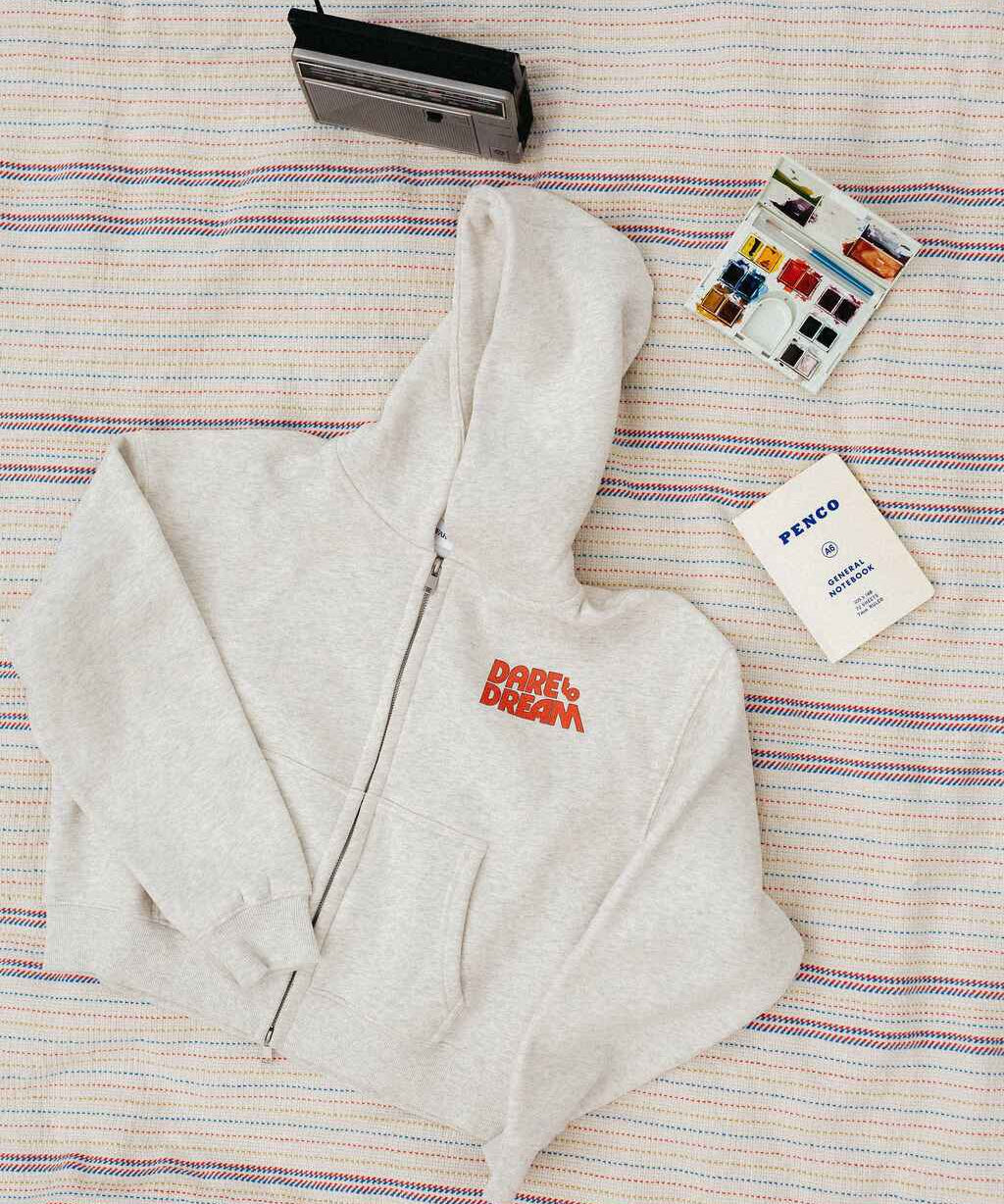 Light gray hoodie with red text that says "dare to dream" on a striped blanket background