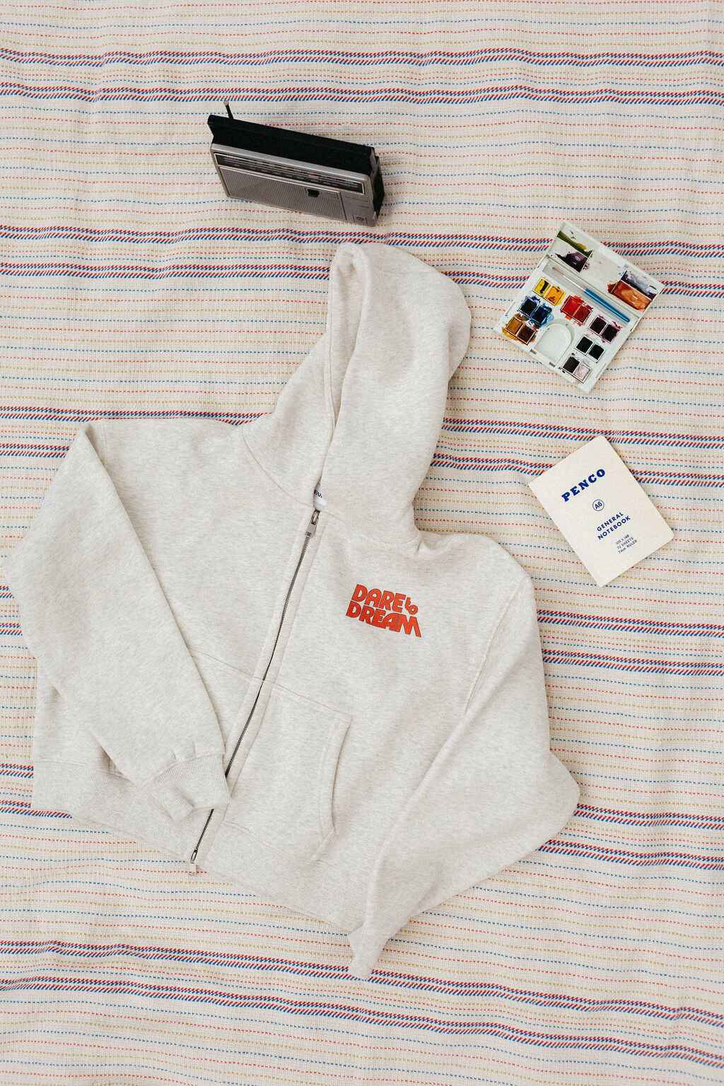 Light gray hoodie with red text that says "dare to dream" on a striped blanket background