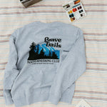 Gray sweatshirt with 'Brave Trails Mountaineering Club' design on a striped blanket background