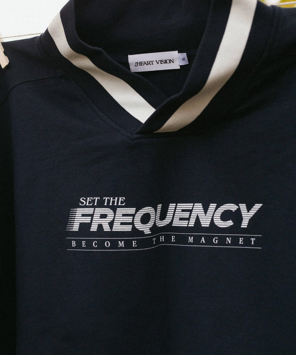 close up view of graphic on front of navy sweater that says "set the frequency become the magnet"