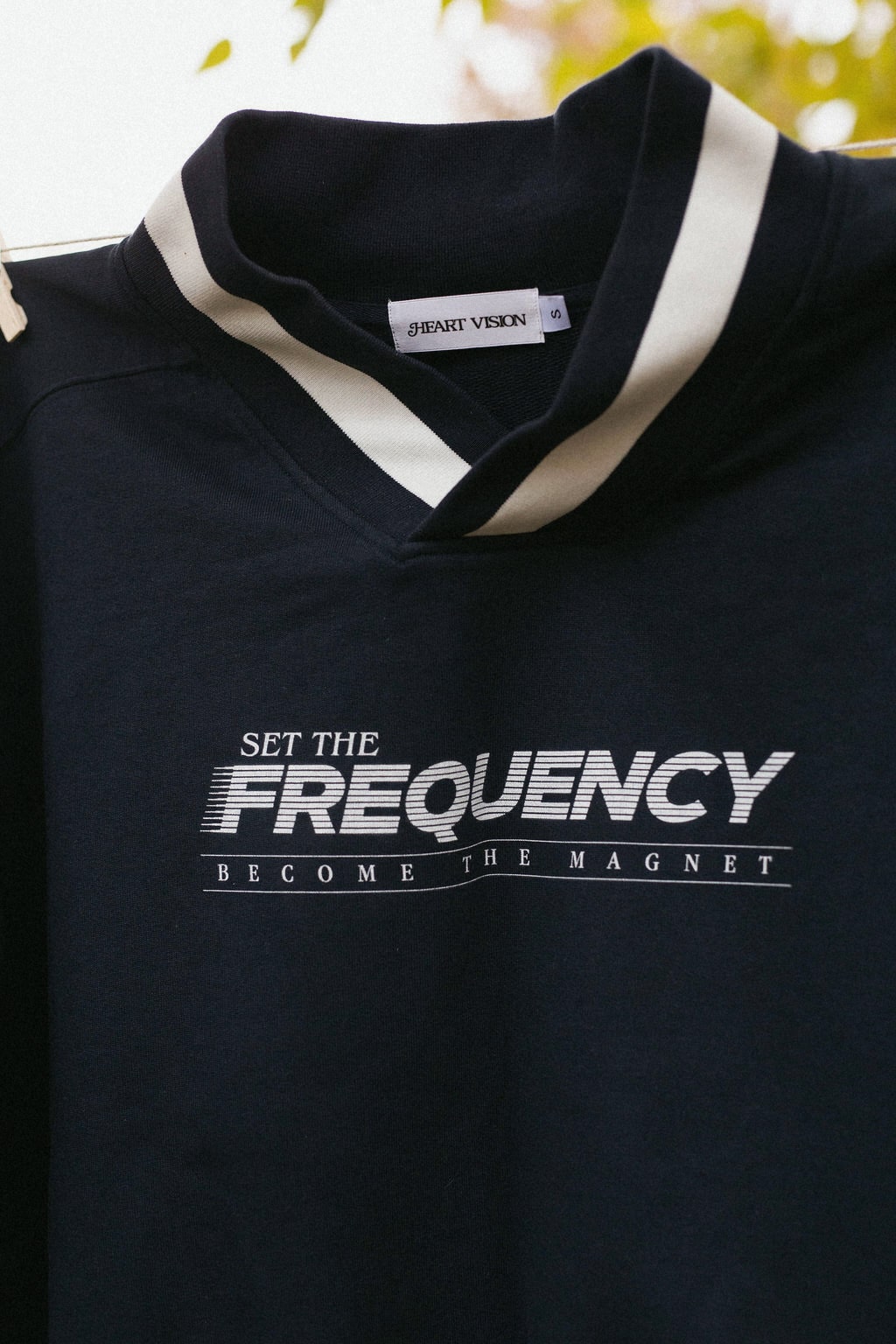 close up view of graphic on front of navy sweater that says "set the frequency become the magnet"