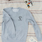 front of gray sweatshirt with brave trails mountaineering club logo on a striped blanket with paints and a radio