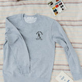 front of gray sweatshirt with brave trails mountaineering club logo on a striped blanket with paints and a radio