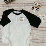Front of white and black baseball shirt with a logo on a striped blanket background