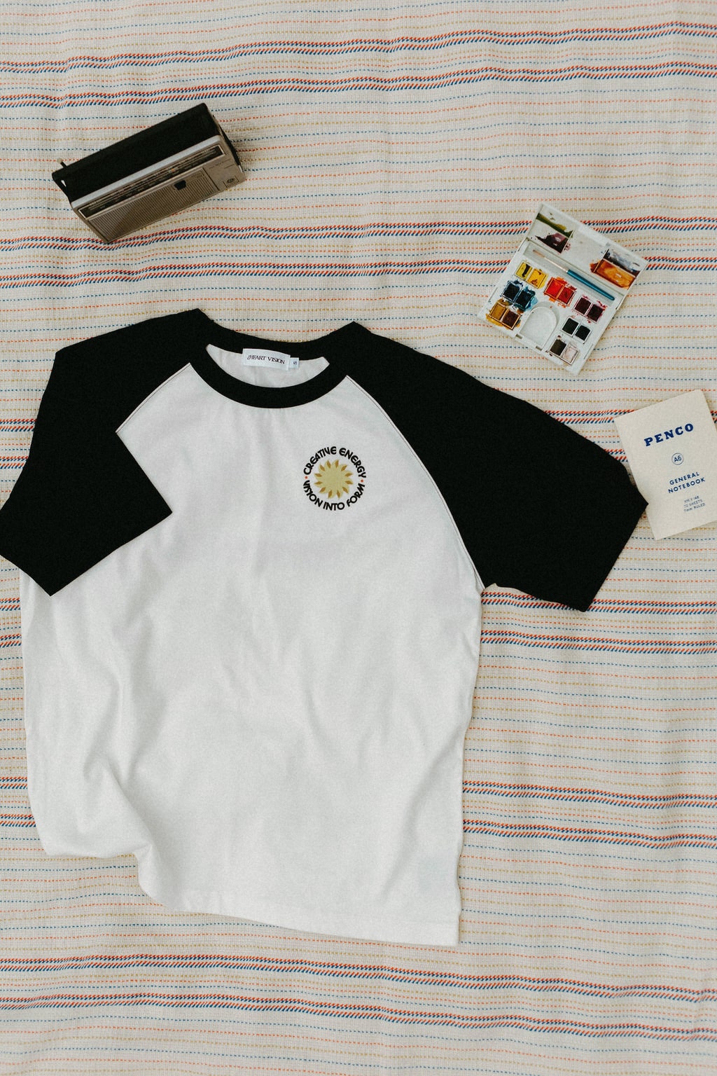 Front of white and black baseball shirt with a logo on a striped blanket background