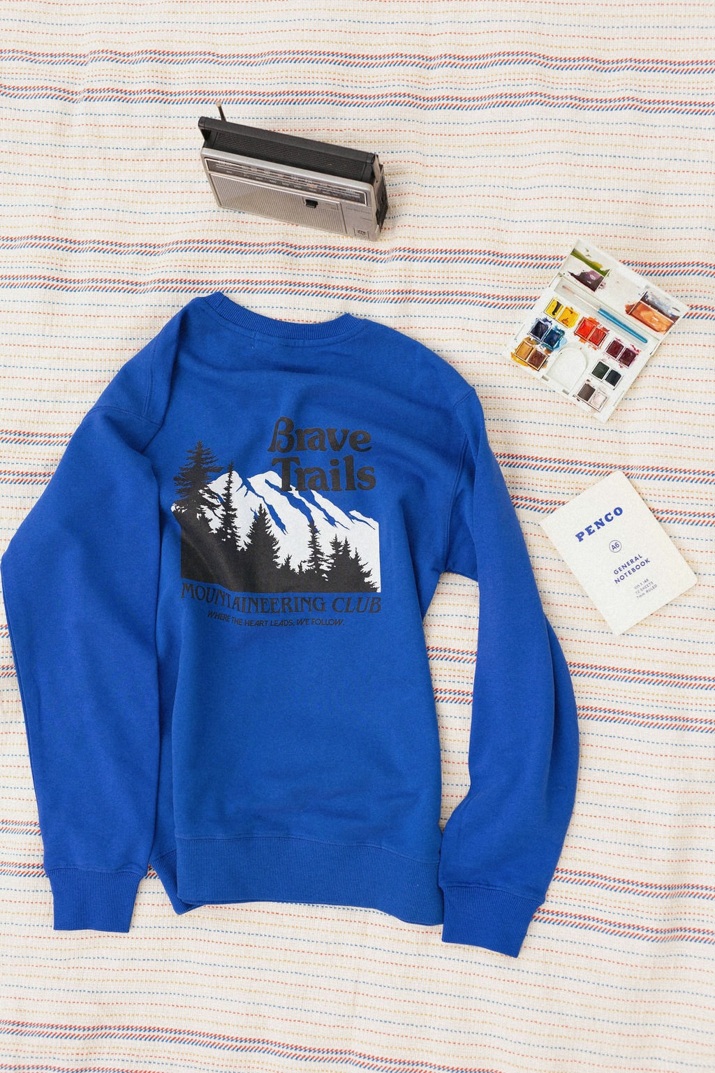 Back of a blue sweatshirt with a mountain graphic on a striped blanket background