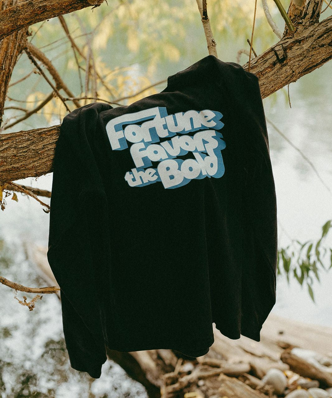 Black long sleeve t-shirt with 'Fortune favors the bold' text hanging on a tree branch