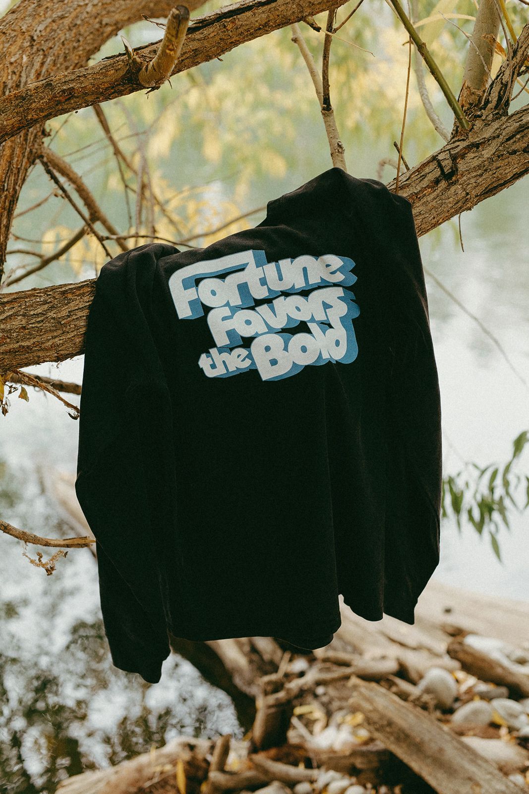 Black long sleeve t-shirt with 'Fortune favors the bold' text hanging on a tree branch