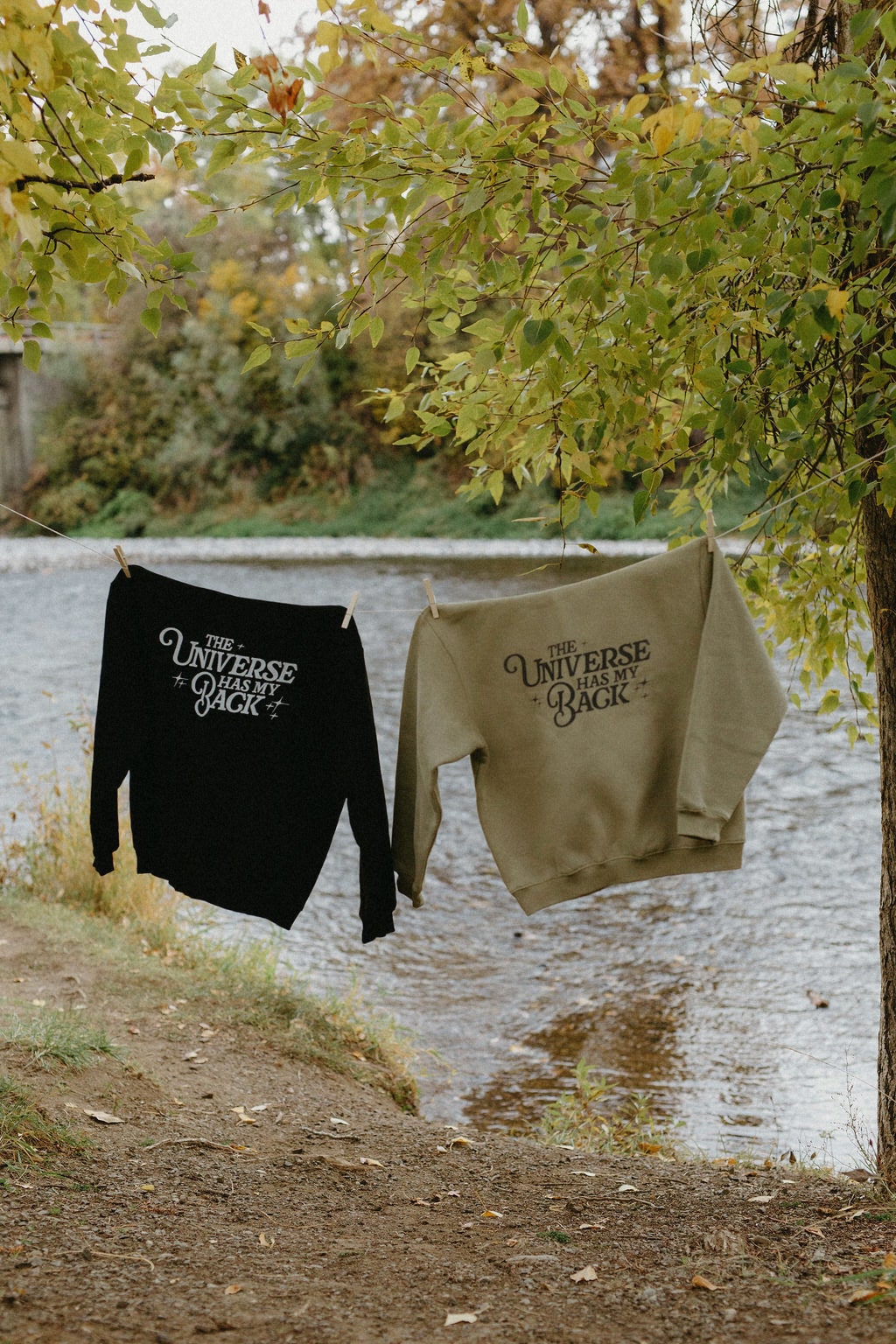 Two sweatshirts with text hanging on a clothesline by a body of water.