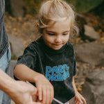 Child wearing a black t-shirt with 'Dare Dream' text, standing outdoors.