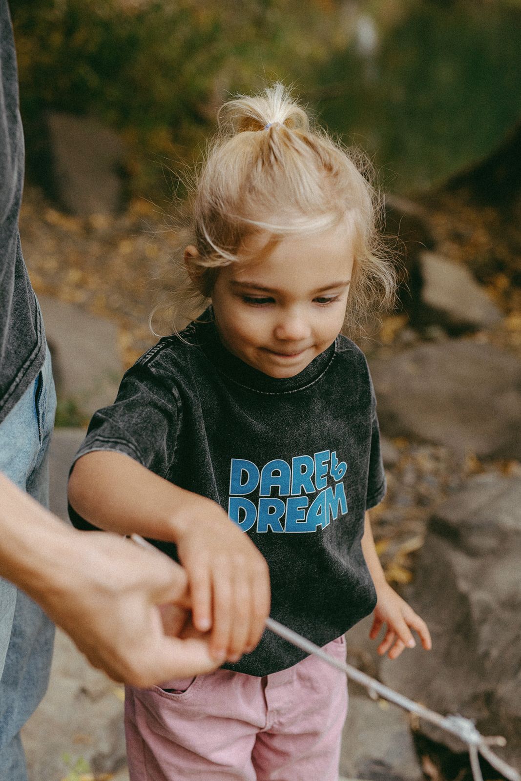 Child wearing a black t-shirt with 'Dare Dream' text, standing outdoors.