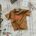 Brown t-shirt with 'Dare to Dream' text on a striped blanket with stationery items.