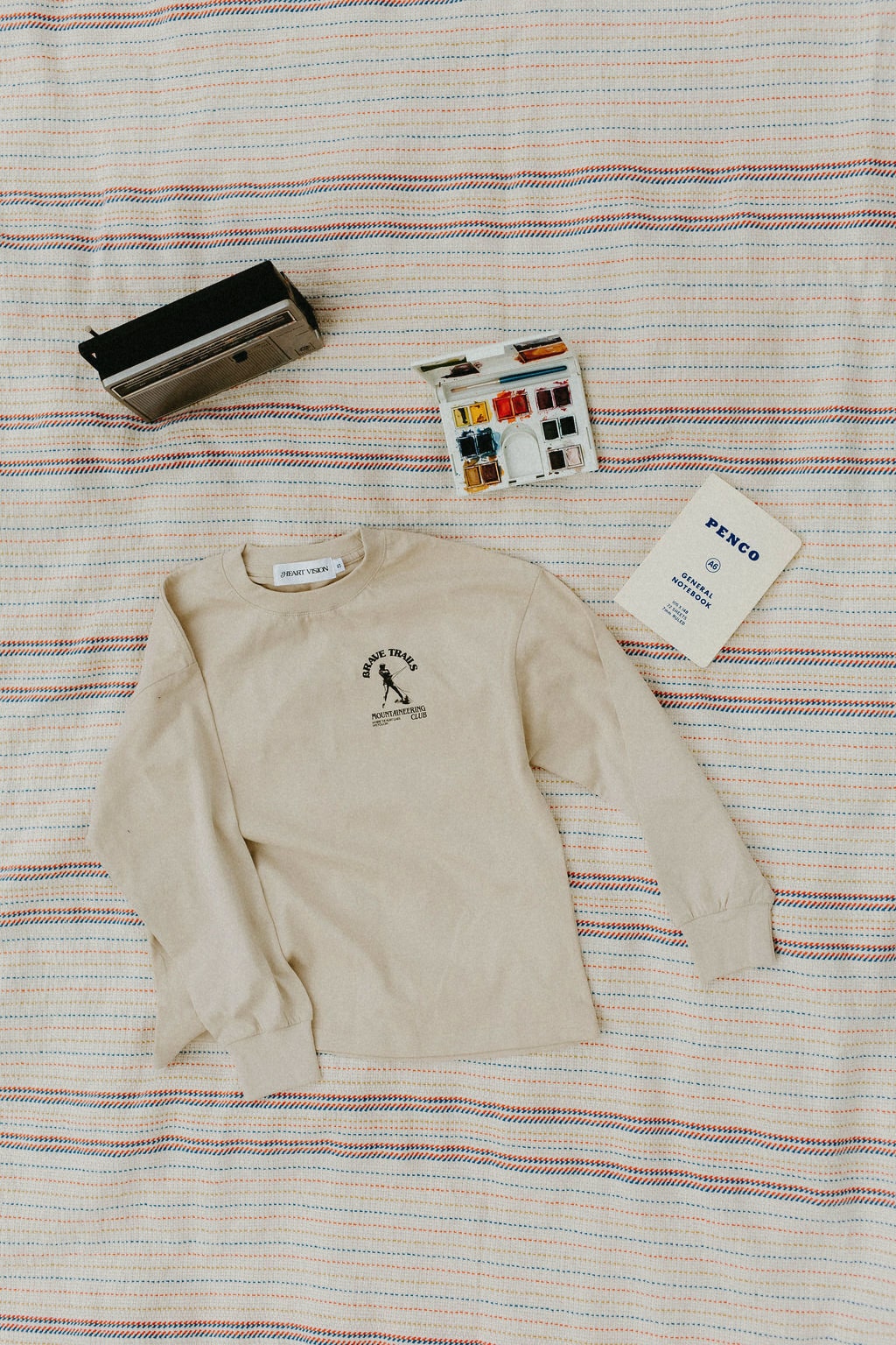 Beige long sleeve t-shirt with a logo on a striped blanket background