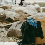 Black t-shirt with 'dare to dream' text draped over a woven basket by a river with people in the background.