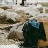 Black t-shirt with 'dare to dream' text draped over a woven basket by a river with people in the background.