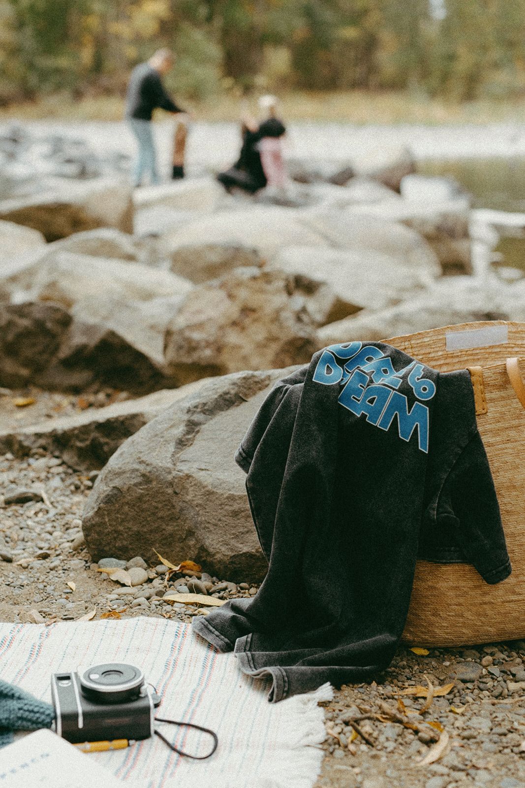 Black t-shirt with 'dare to dream' text draped over a woven basket by a river with people in the background.