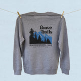 Back of gray sweatshirt with 'Brave Trails Mountaineering Club' design hanging on a clothesline on a light blue background