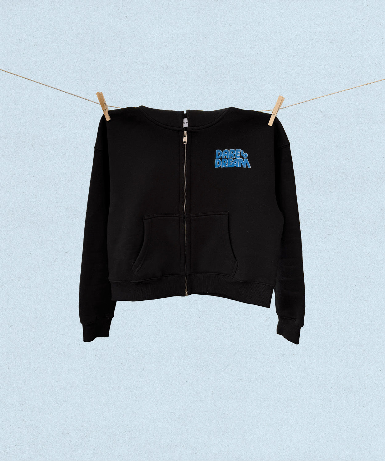 Black hoodie with blue text that says "dare to dream" on a clothesline against a light blue background