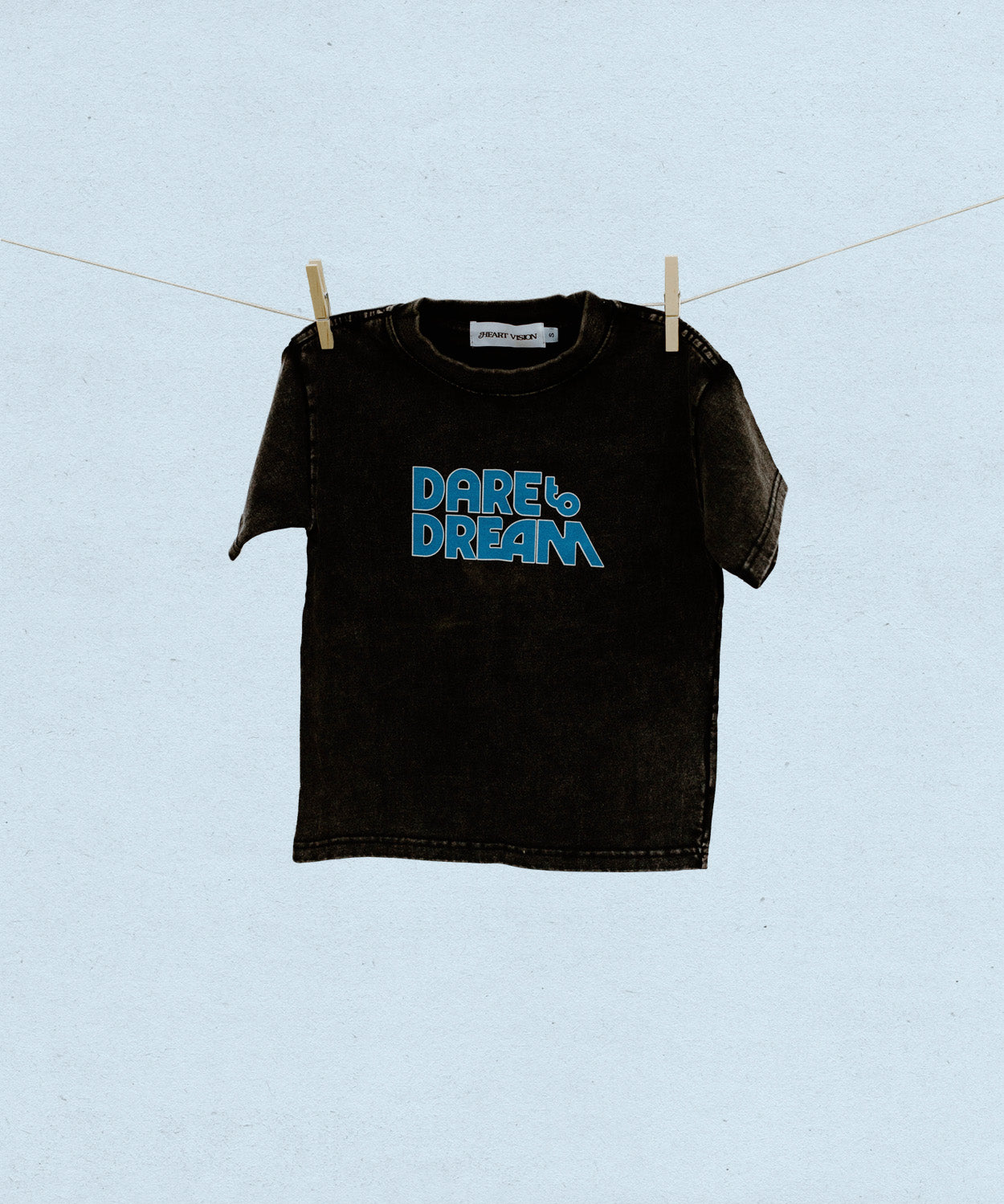 Black t-shirt with blue 'Dare to Dream' text on a clothesline against a light blue background