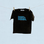 Black t-shirt with blue 'Dare to Dream' text on a clothesline against a light blue background
