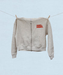 Beige hoodie with red text 'Dare to Dream' hanging on a clothesline against a light blue background