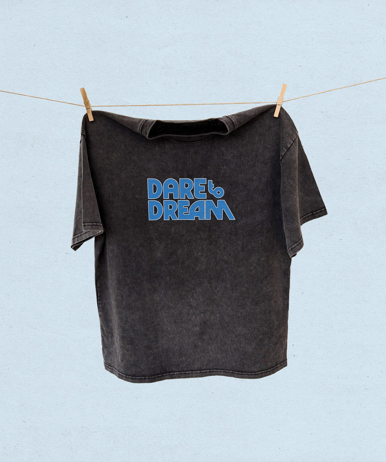 Black t-shirt with 'Dare to Dream' text on a clothesline against a light blue background