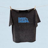 Black t-shirt with 'Dare to Dream' text on a clothesline against a light blue background