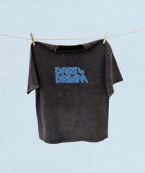 Black t-shirt with 'Dare to Dream' text on a clothesline against a light blue background