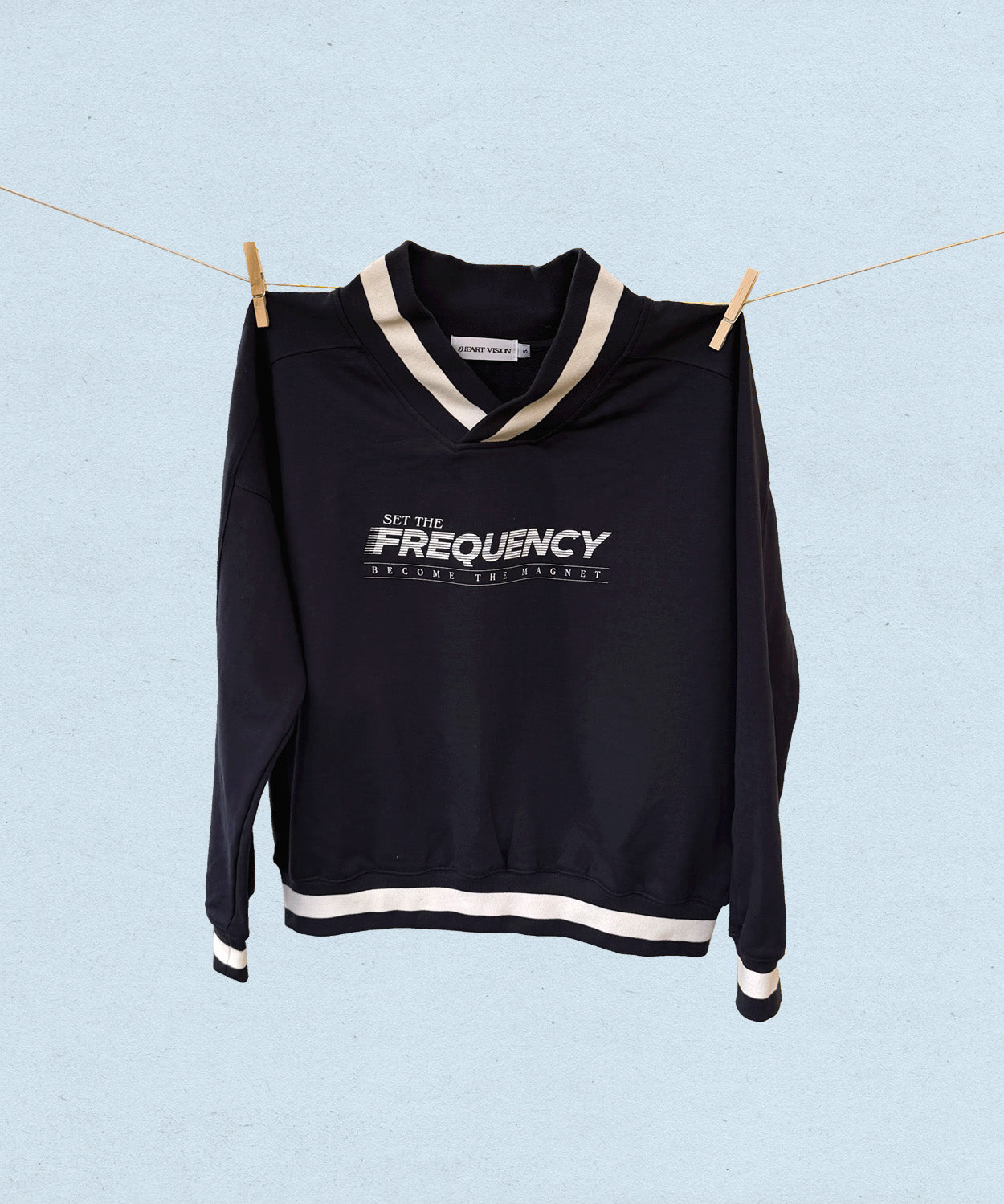 Navy sweater with white trim and  'Set the Frequency, become the magnet' text on a light blue background
