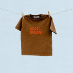 Brown t-shirt with red/orange 'Dare Dream' text on a clothesline against a light blue background