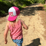 Child wearing the Shine On pink and white youth trucker hat on a forest trail