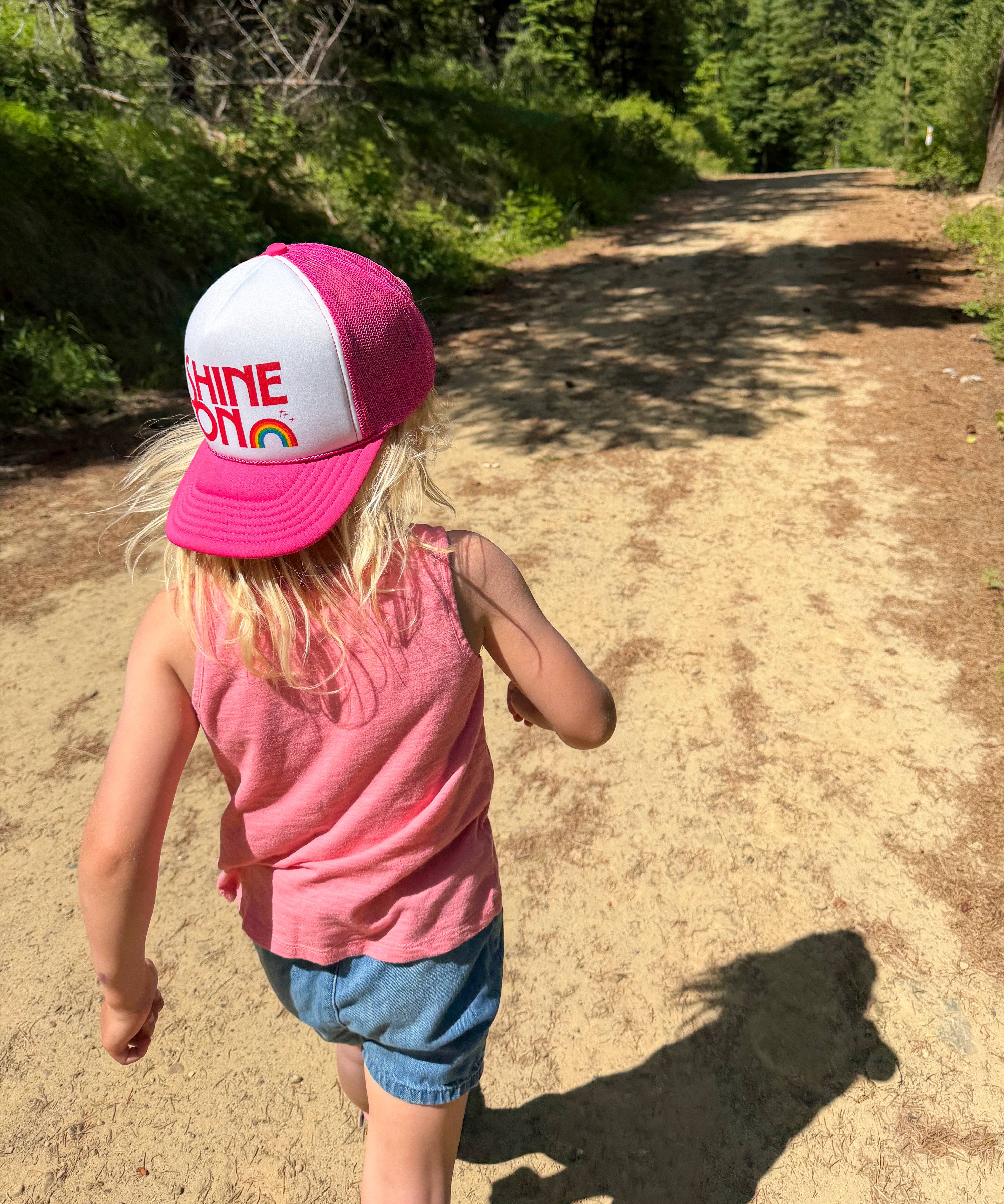 Child wearing the Shine On pink and white youth trucker hat on a forest trail